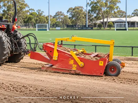 Red-and-yellow scraper grading beside hockey field — application concept